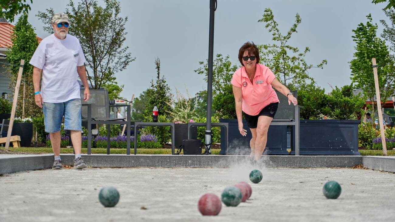 A woman throwing a bocce ball in the sand court on the Amblebrook great lawn.