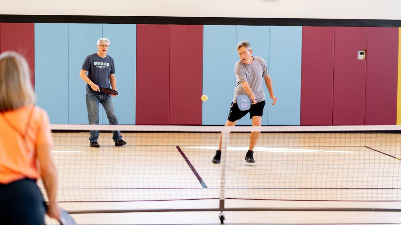 Two men playing partners pickleball on an indoor pickleball court.