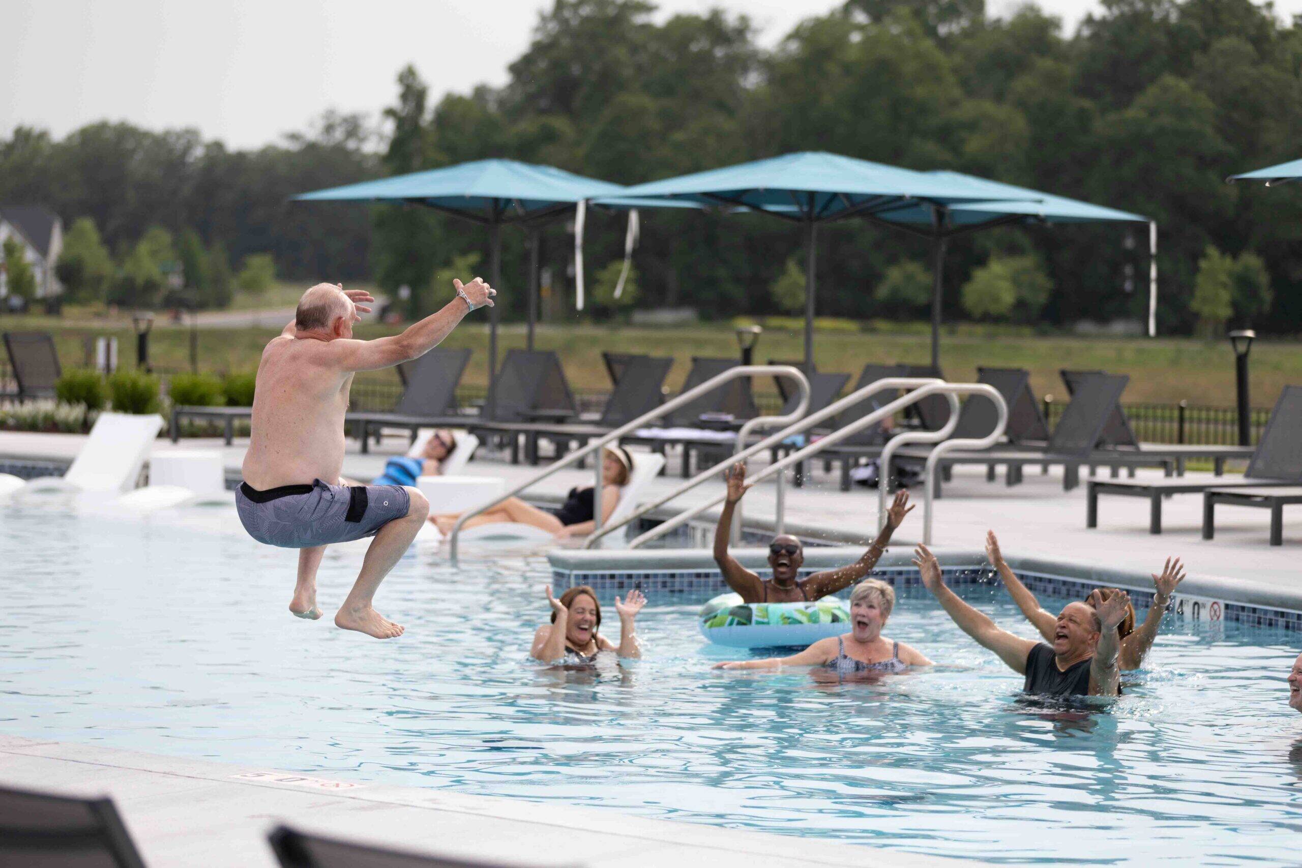 Active adult community pool with retired man doing a cannonball while his friends cheer him on 