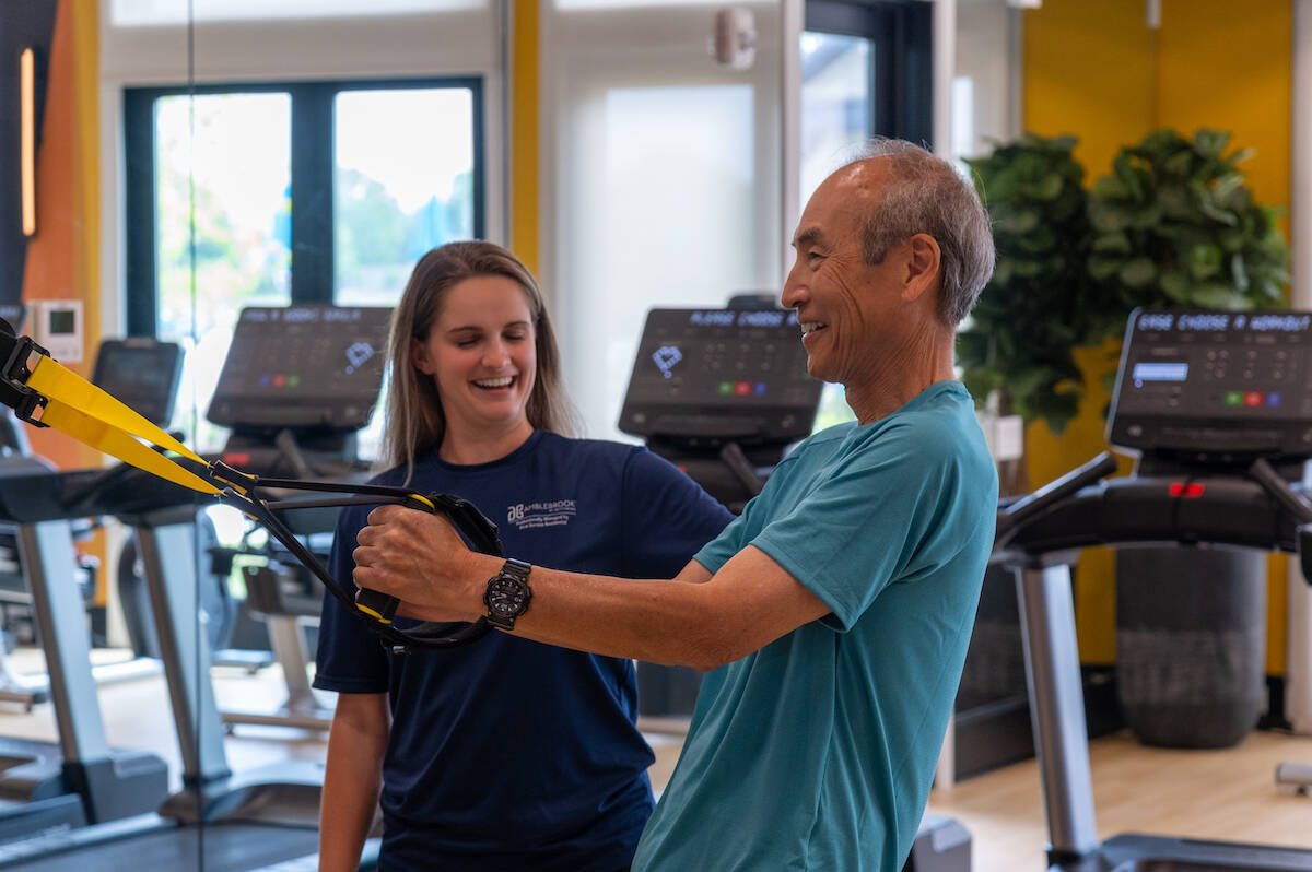 A fitness instructor demonstrates exercises to a man learning in a gym setting, both engaged in an active training session.